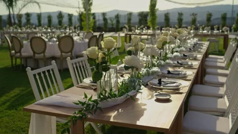 Long wedding table with white roses and gold cutlery on lawn at sunset 動画素材 344512238