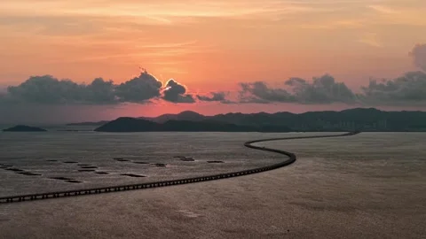 Long winding bridge over calm sea water with distant hills at sunset Stock-Footage 344954013