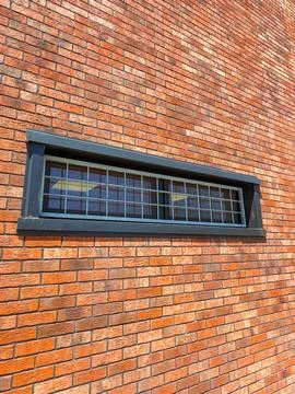 A long window with a black frame is seen on a red brick wall. The window is c Stock Photos