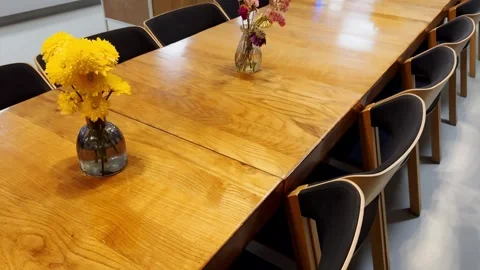 Long wooden dining table with chairs and small flower vases in a bright café or Stock Footage 338003397