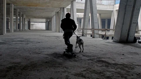 A longboarder is pulled by a dog that comes from a shadow in an abandoned object Stock Footage 90209298
