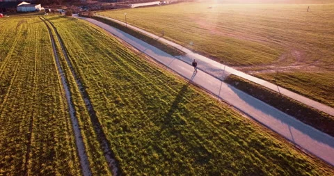 Longboarder skating down the road at sunset though field 스톡 동영상 153518986
