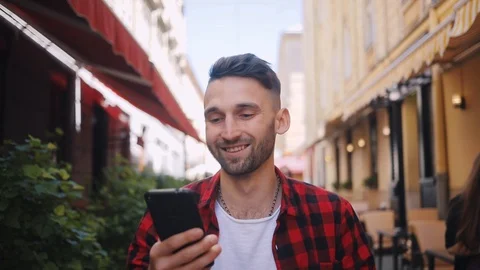 Look at camera young man with blue eyes uses phone walk in city smile feel happy Stock Footage 92071566