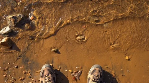 A look down view of waves washing up against hiking boots. Stock Footage 119334843