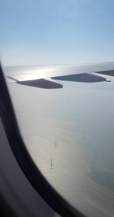 Look out from passenger plane window, wing, ocean with turbines below Stock Footage 297053560