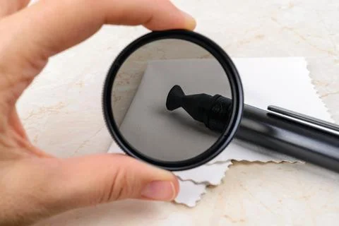 Look through a clean camera polarizing filter at lens pen on a white microfiber Stock Photos
