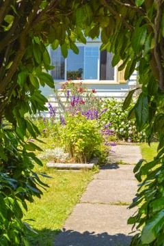 Look through the green gate on the pathway leading to a house with flowers Stock Photos