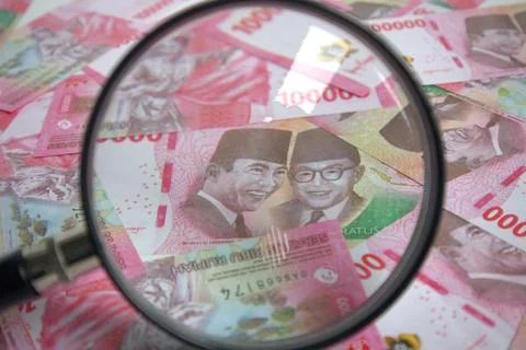 Look using a magnifying glass at the stack of rupiah bills Stock Photos