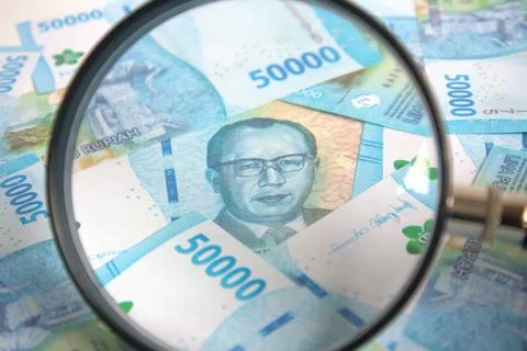 Look using a magnifying glass at the stack of rupiah bills Stock Photos