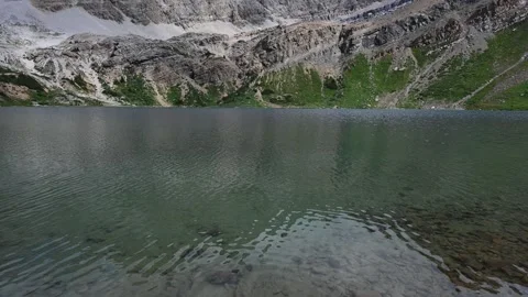 Looking across a mountain lake with gentle waves reflecting rugged cliffs in a Stock Footage 333074859