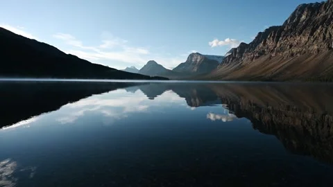 Looking across a very calm mountain lake surrounded by rocky mountains under blu Stock Footage 302207279