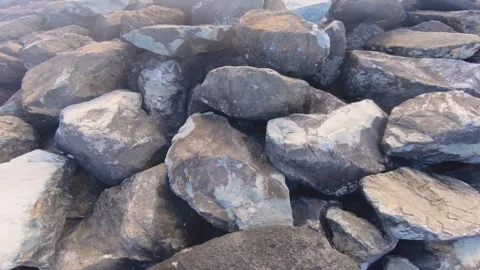 Looking around big boulder pill of rocks at coastline protection from lagoon ato Stock Footage 258443822