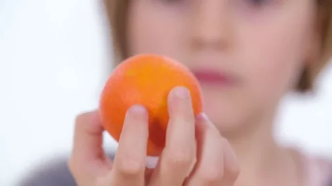Looking closely at a small tangerine in her hand Stock Footage 83725019
