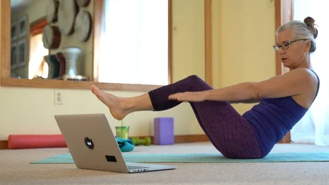 Looking at a computer laptop screen a mature woman does V-ups or sit-ups while Stock Footage 128639337