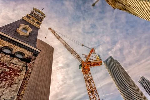 Looking up at a crane between a clock tower and a skyscraper.` 写真素材