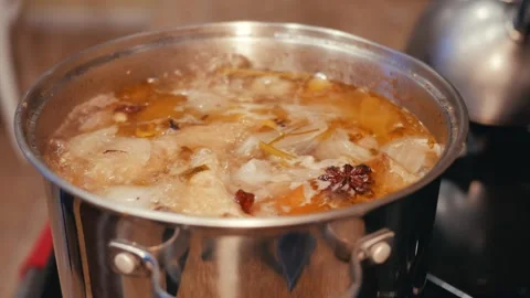 Looking down at chicken stock boiling in a stainless steal pot Stock Footage 257471912