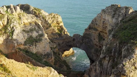 Looking down from cliff to natural stone arc from ocean Stock Footage 273674141