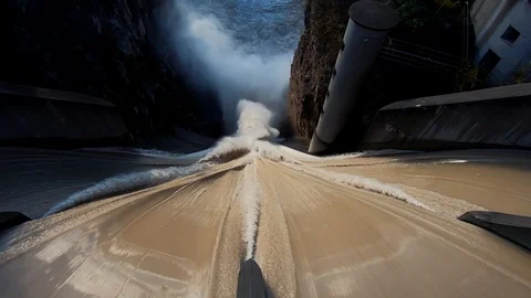 Looking down dirty brown flooded water flows over concrete spillway Stock Footage 120922300