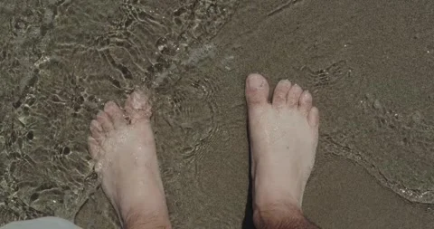 Looking down at feet on a sandy beach in shallow water Stock Footage 310573581
