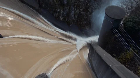 Looking down left pan over dam with brown flooded water Video stock 120033563