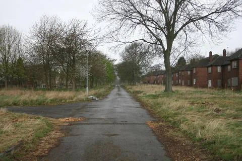 Looking Down Overgrown Road With Boarded Up Houses In Abandoned British Town Stock Photos