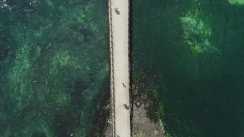 Looking down at a person walking on a bridge over the blue sea with a drone. Stock Footage 136644305