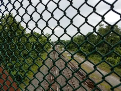 Looking down at railroad tracks through metal fence Stock Photos