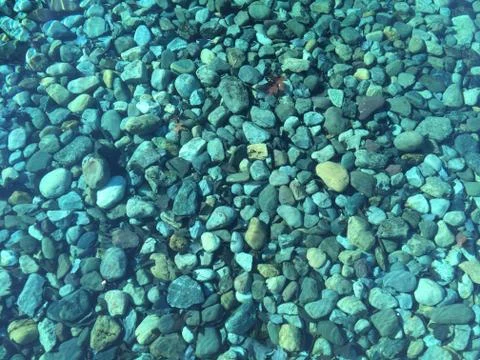 Looking down at rocks in a pond with clear blue water, aqua blue rocks, backg Stock Photos