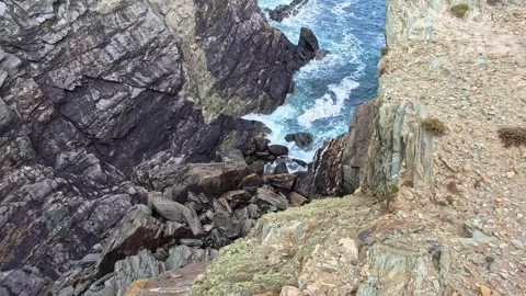 Looking down rocky steep Welsh ocean coastline to crashing waves below Видео 337924269