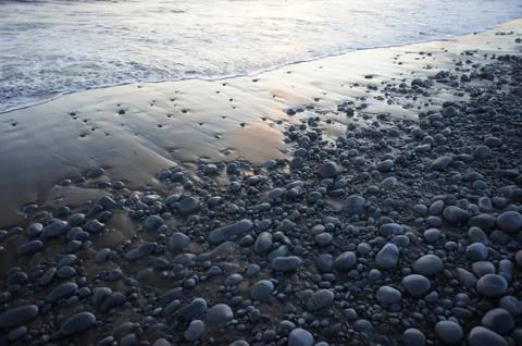 Looking down at a stone covered beach as the gentle waves wash up on the sand Stock Photos