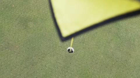 Looking down a yellow and black flagstick to a putting green and cup on a beauti Stock Footage 305476093