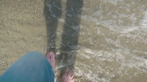 Looking down at your bare feet as you walk along the brown sand beach washed by Vidéo 172034849