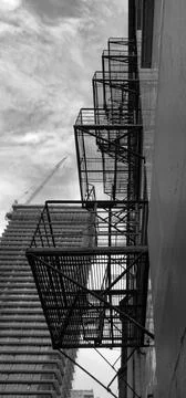 Looking up at fire escape attached to building as skyscrape is built in the.. Stock Photos