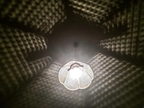 Looking up at glowing lamp hanging from the ceiling with shadows Stock Photos