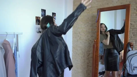 Is looking in a mirror putting on lather jacket in wardrobe talking on phone Video stock 148125042