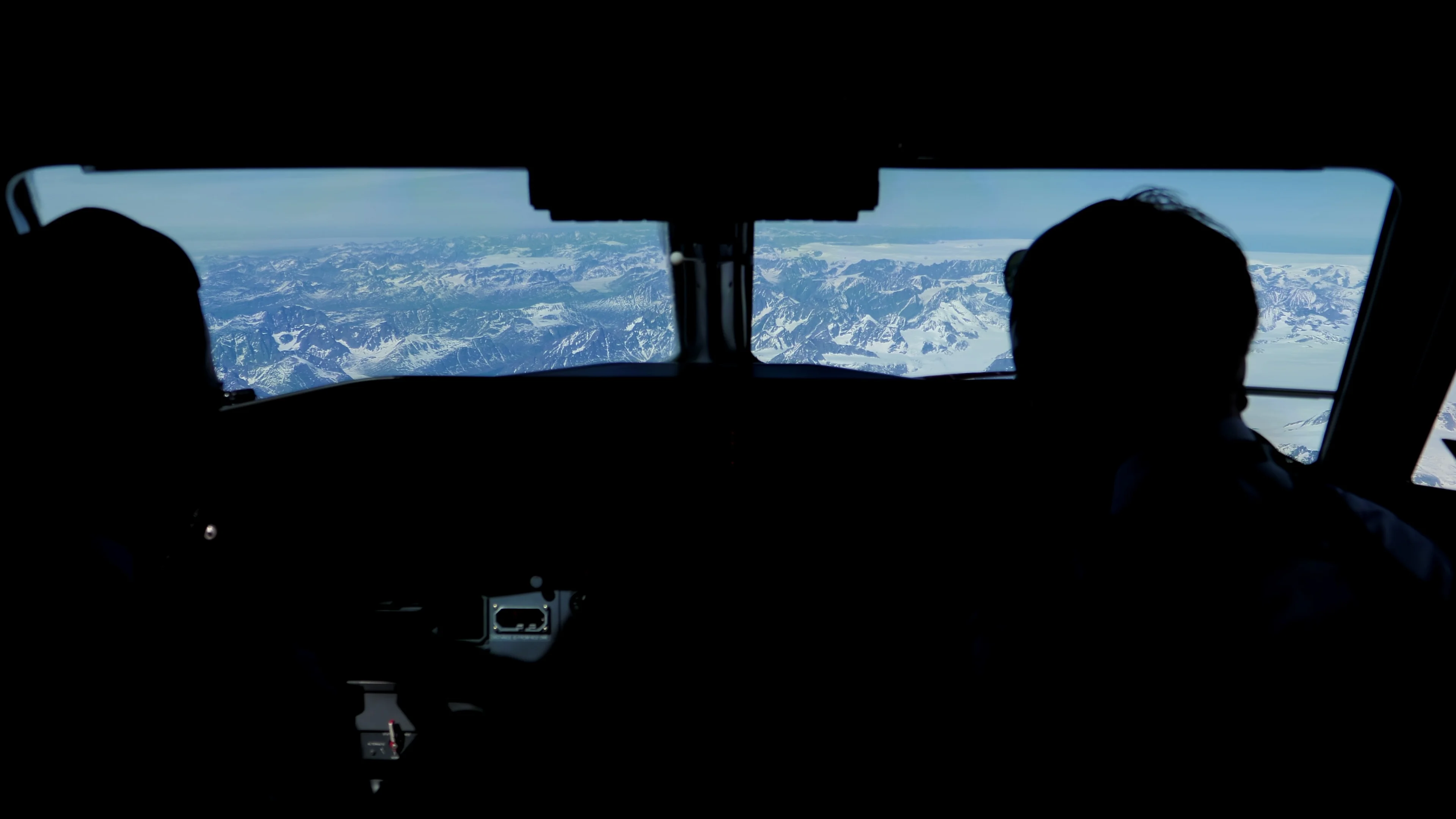 Looking out pilot cockpit window, flying over snowy mountains, Greenland