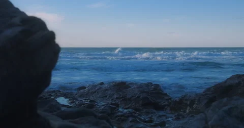 Looking out to sea waves crash from behind rocks on shore, slider 動画素材 151523255