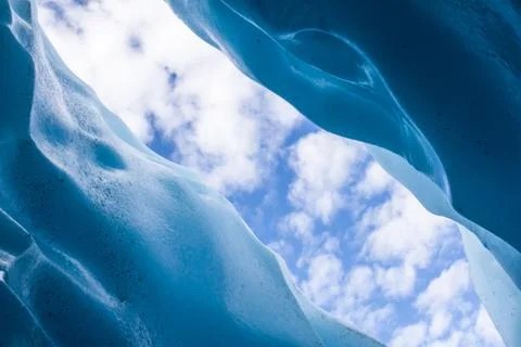 Looking up to a partly cloudy sky through a skylight into an ice cave. Stock Photos