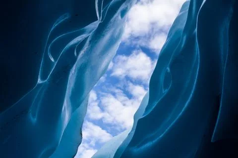 Looking up to a partly cloudy sky through narrow walls of a crevasse. Stock Photos