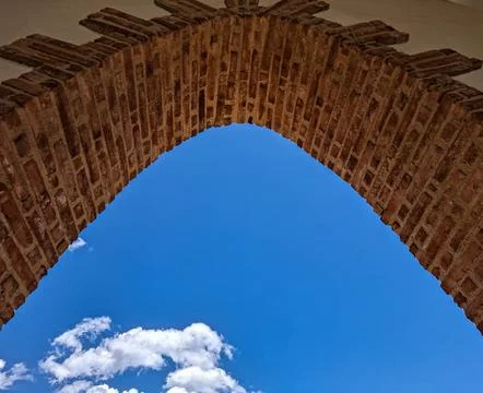 Looking up at a rustic red brick arch against a blue sky with white clouds .. Stock-Fotos