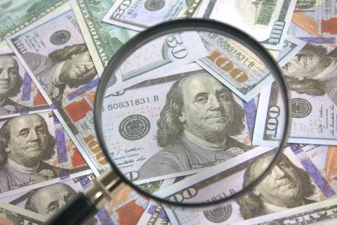 Looking at a stack of 100 dollar bills using a magnifying glass Stock Photos
