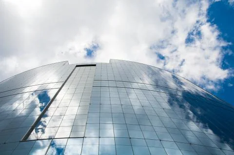Looking up the tall skyscraper with sky reflected in glass walls Stock Photos