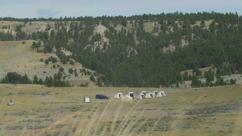 Looking through blowing grass at campsite with group of tents Stock Footage 74789207