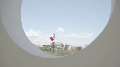 Looking through a circular window at the Mexican flag blowing in slow motion. 스톡 동영상 244822886
