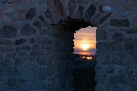 Looking through door in old stone brick wall of castle ruin with setting full Stock Photos