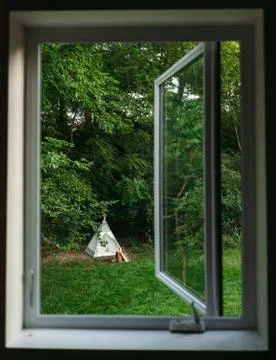 Looking through an open window to a backyard campsite with campfire and teepee Stock Photos