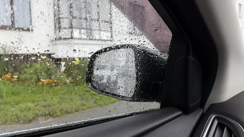 Looking through a wet car window with rain drops at a side mirror and a blurred Stock Photos