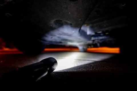 Looking under a SUV at night with a flashlight to inspect problems Foto stock
