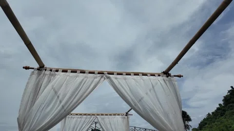 Looking up at a white canopy with curtain against a cloudy sky on a tropical day Video stock 343397067