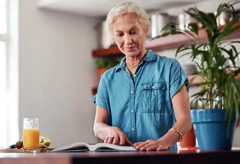 This looks like a goodie...an attractive senior woman reading from a recipe book Stock Photos